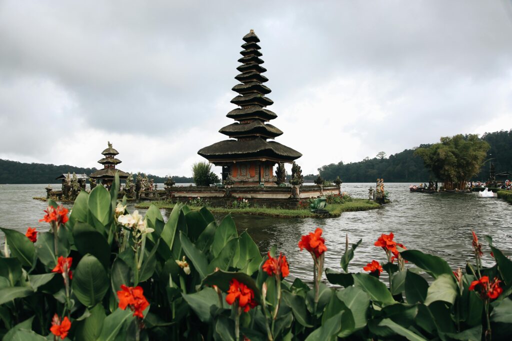 Serene view of Ulun Danu Beratan Temple in Bali with vibrant flowers in the foreground.
